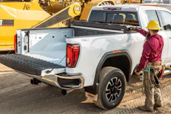 Construction worker in yellow hard hat standing beside white GMC pickup truck with open bed on job site with yellow CAT bulldozer