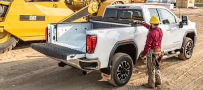 Construction worker in yellow hard hat standing beside white GMC pickup truck with open bed on job site with yellow CAT bulldozer