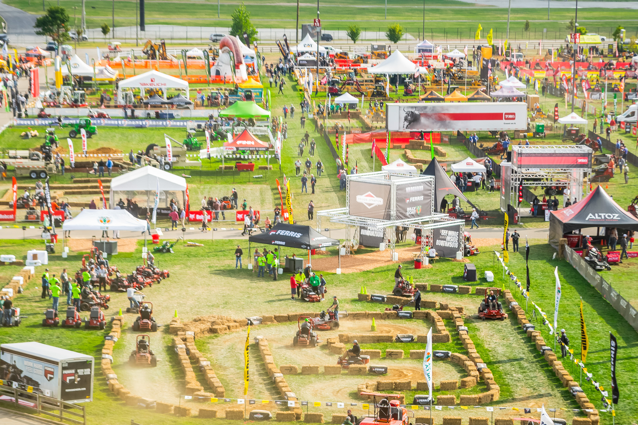 Aerial view of agricultural equipment exhibition with multiple vendor tents, machinery displays, and attendees on green field