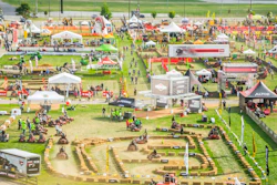 Aerial view of agricultural equipment exhibition with multiple vendor tents, machinery displays, and attendees on green field
