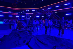 Neon-lit indoor venue with blue and pink lighting, people gathered under illuminated architectural structures