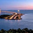 Vasco da Gama Bridge illuminated at dusk with calm blue water and distant cargo ship