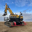 Yellow and black mobile excavator with articulated crane arm and red hydraulic outriggers on barren landscape