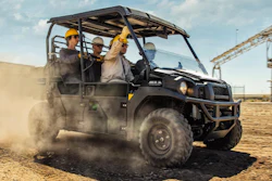 Workers in hard hats operate a black utility vehicle across dusty terrain on a construction site