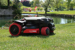 Red and black robotic lawn mower with ZEROTRIM branding on grass by a river