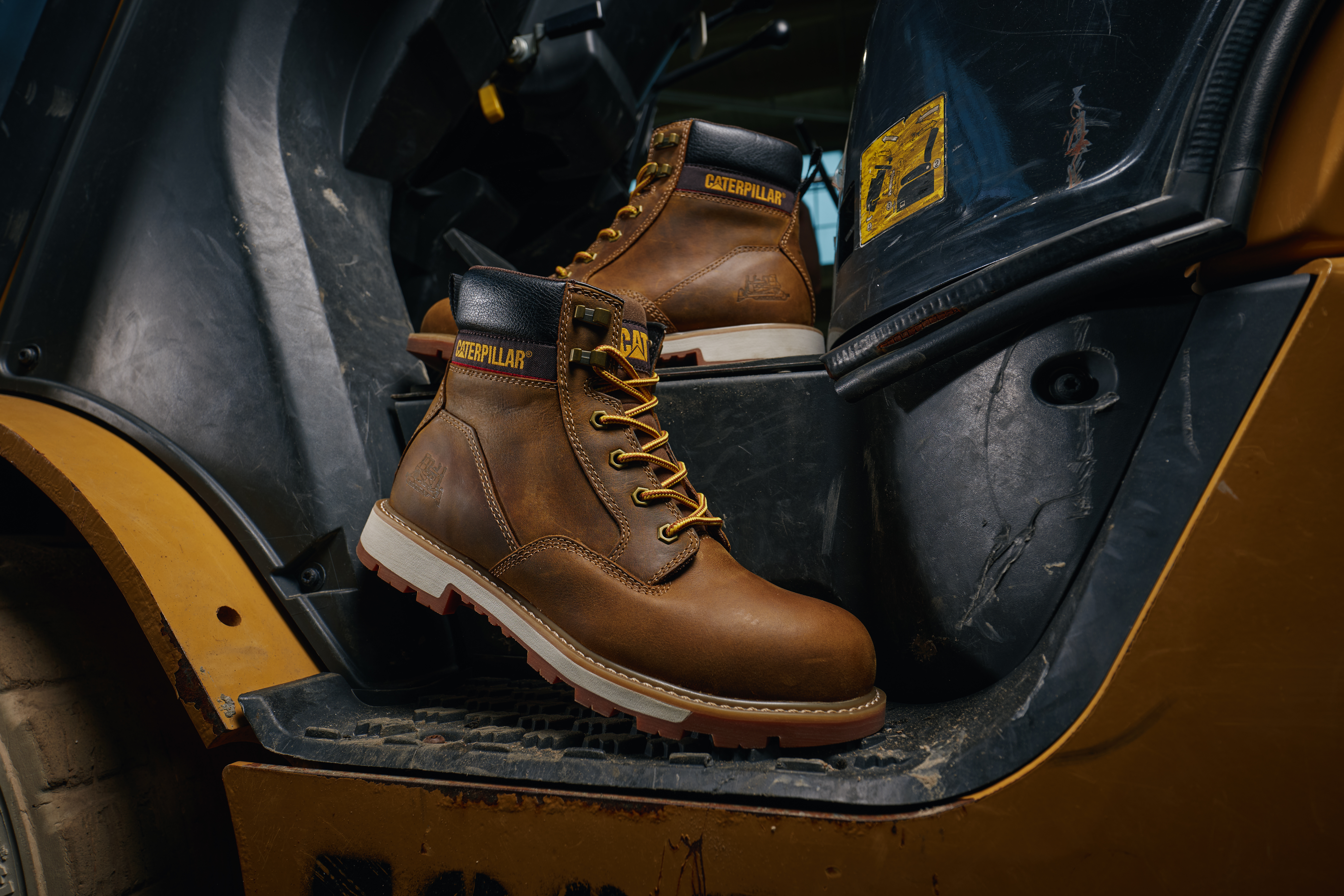 Caterpillar brown leather work boot with lace-up design displayed on yellow heavy machinery