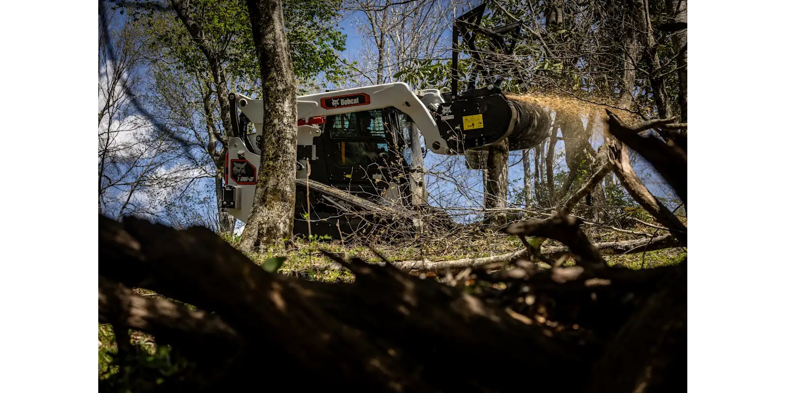 Bobcat skid-steer loader with forestry attachment clearing branches among trees