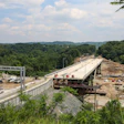 Highway construction site with new bridge infrastructure and earthwork surrounded by dense forest canopy