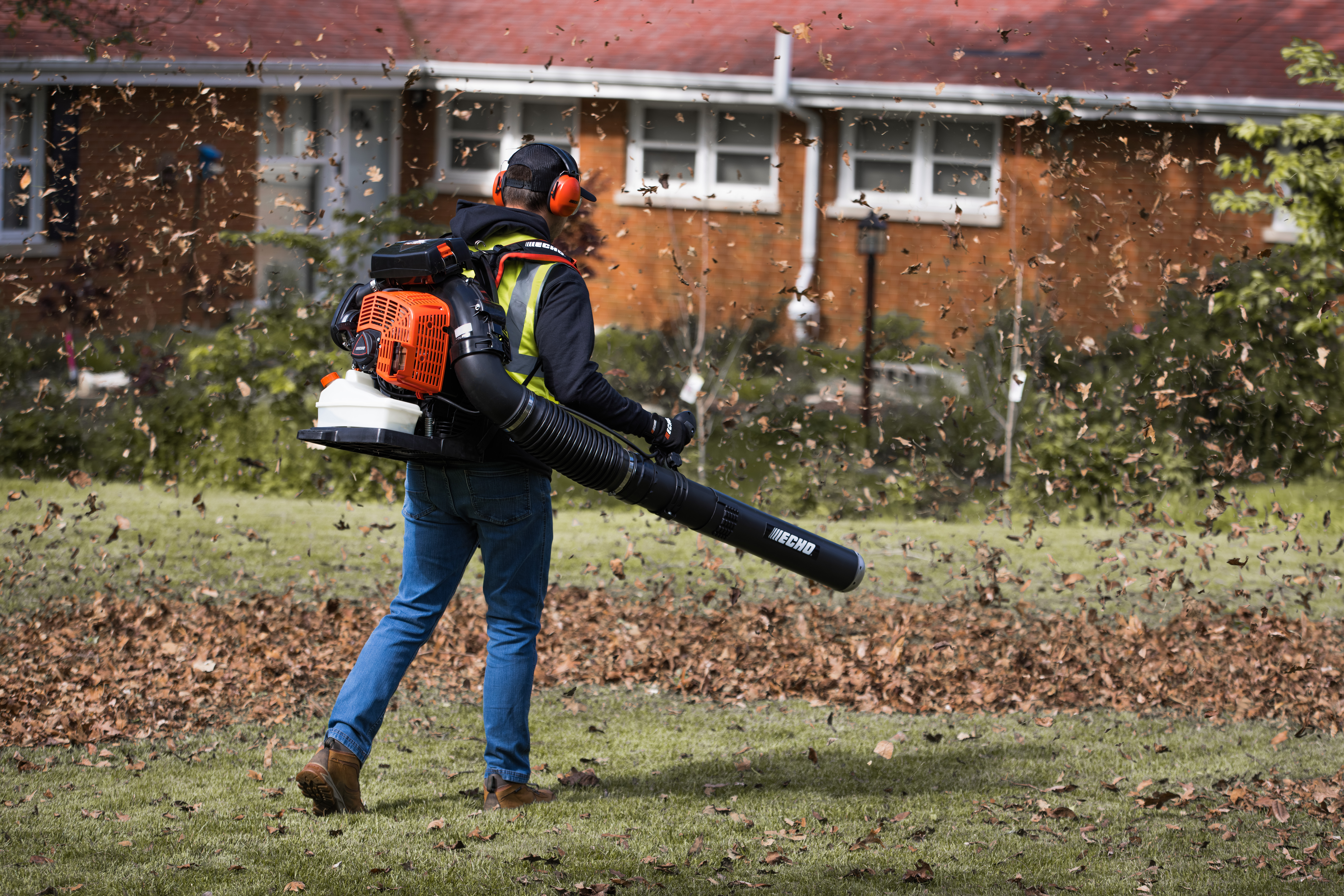 Worker using a leaf blower to clear leaves from residential yard