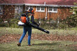 Worker using a leaf blower to clear leaves from residential yard