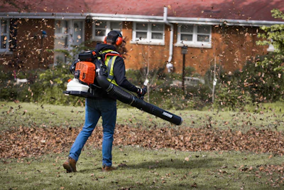 Worker using a leaf blower to clear leaves from residential yard