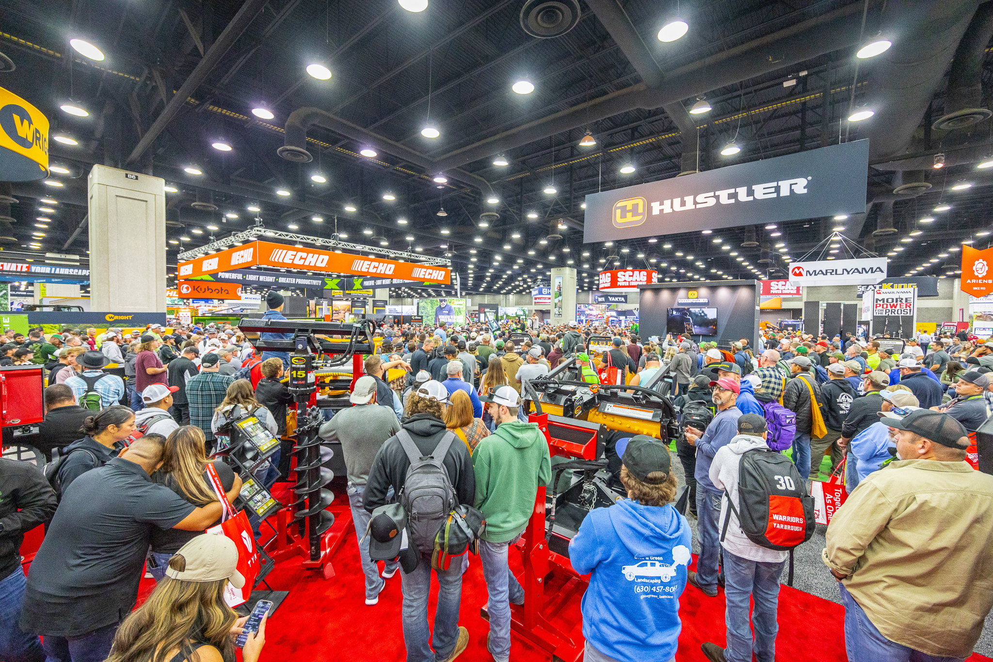 Crowded trade show floor with hundreds of attendees browsing equipment and product booths under bright overhead lighting