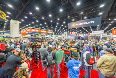 Crowded trade show floor with hundreds of attendees browsing equipment and product booths under bright overhead lighting