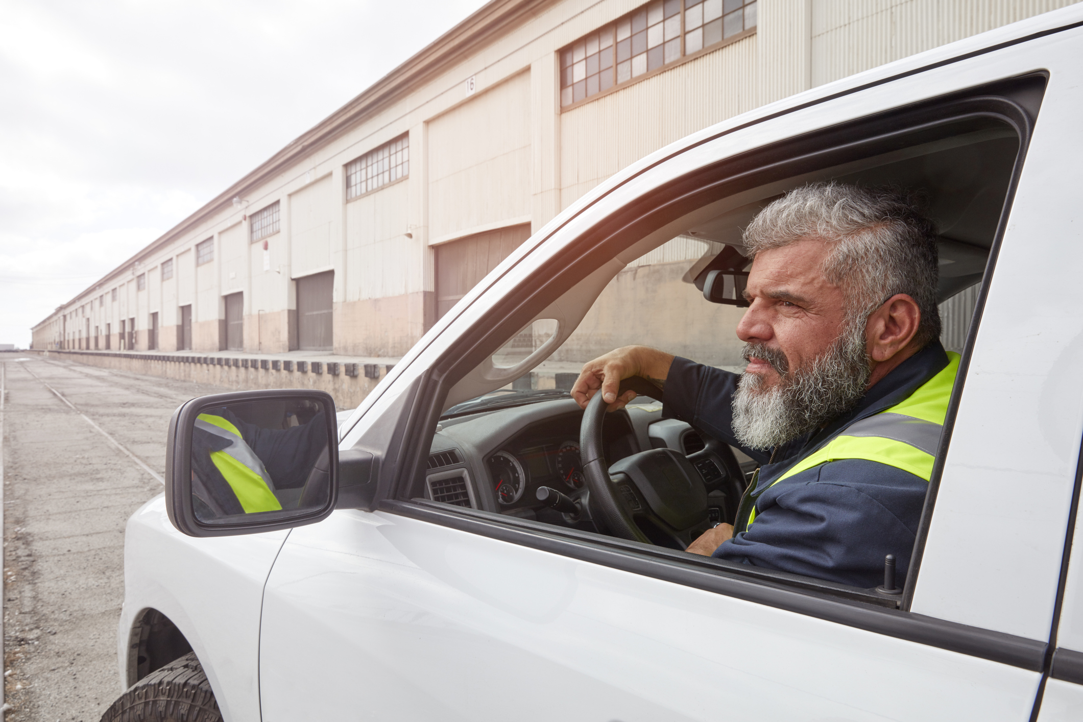 Delivery driver in high-visibility vest sitting in white van at industrial warehouse
