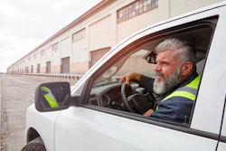 Delivery driver in high-visibility vest sitting in white van at industrial warehouse