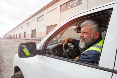 Delivery driver in high-visibility vest sitting in white van at industrial warehouse
