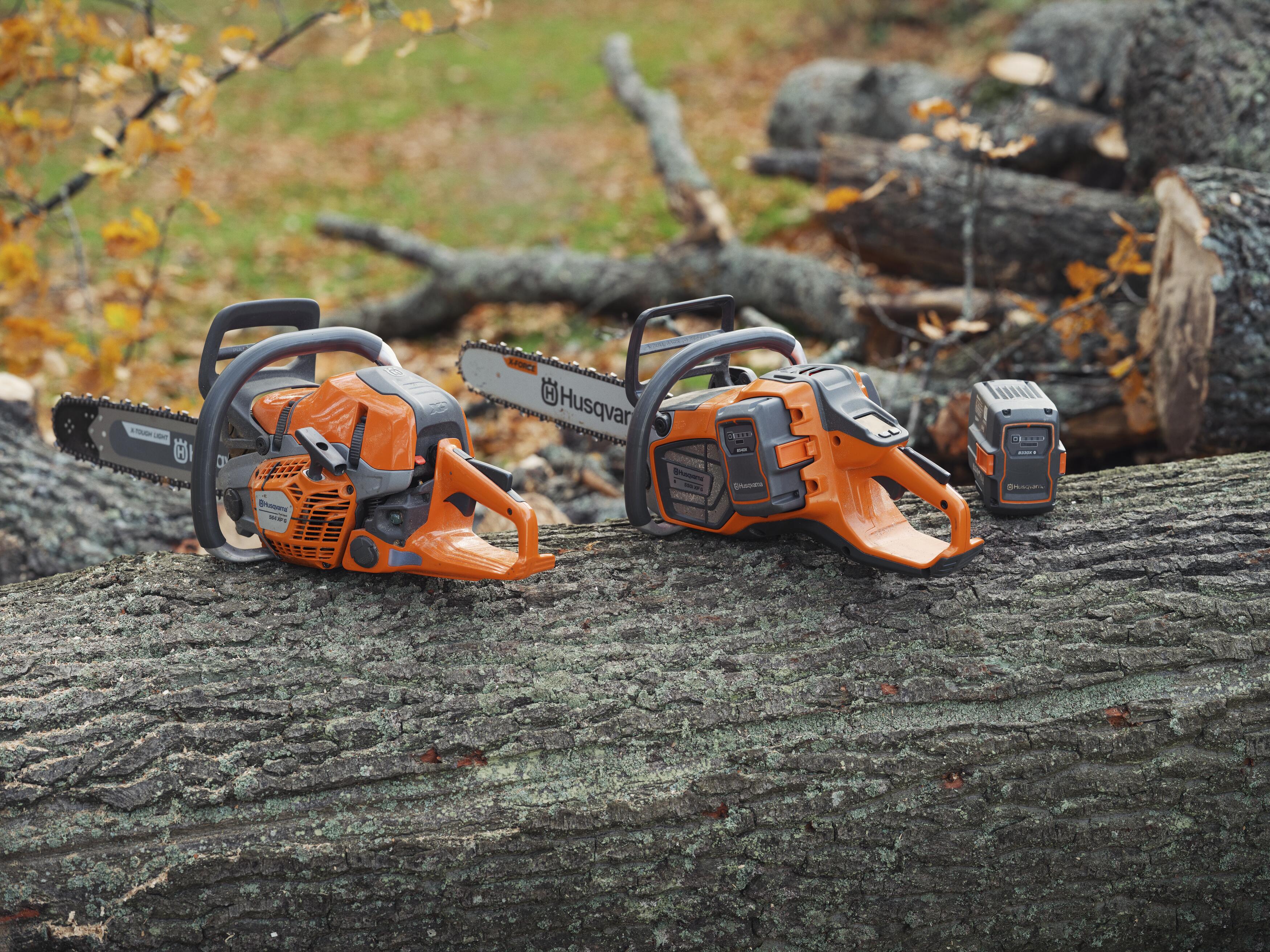 Two orange and black Husqvarna chainsaws positioned on a weathered log with forest debris in background