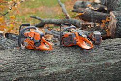 Two orange and black Husqvarna chainsaws positioned on a weathered log with forest debris in background