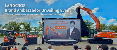 LANDCROS brand ambassador unveiling event featuring Hitachi construction machinery with orange excavators and promotional signage