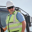 Construction worker wearing safety gear and hard hat standing beside work vehicle