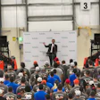 Kubota corporate event with speaker addressing crowd near red construction equipment and branded backdrop
