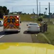 Emergency ambulance with flashing lights on highway surrounded by vehicles and grassy median
