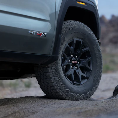 Black GMC truck with all-terrain tires and dark alloy wheels parked on gravel road