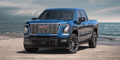 Blue GMC Sierra pickup truck parked on sandy beach with ocean waves in background