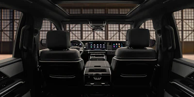 Luxury vehicle interior with black leather seats, digital dashboard, and panoramic windshield view of industrial building