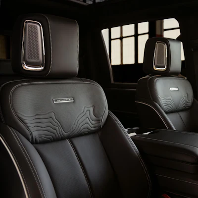 Luxury vehicle interior with black leather seats, embossed headrests, and gridded windows in background