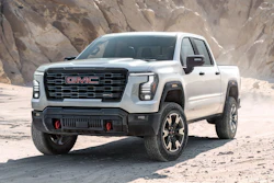 White 2027 GMC Sierra 1500 pickup truck parked on desert terrain with rocky cliff backdrop