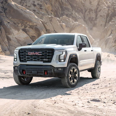 White 2027 GMC Sierra 1500 pickup truck parked on desert terrain with rocky cliff backdrop