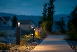 Illuminated pathway through a residential garden at twilight with modern bollard lights and mountain backdrop
