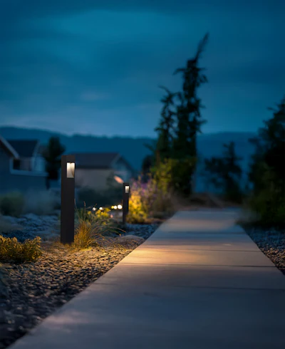 Illuminated pathway through a residential garden at twilight with modern bollard lights and mountain backdrop