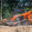 Orange Develon DTL26 skid steer compact track loader operating on sandy construction site with traffic cone nearby