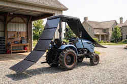 Blue tractor with extended solar panel canopy parked at rural farmhouse with stone buildings