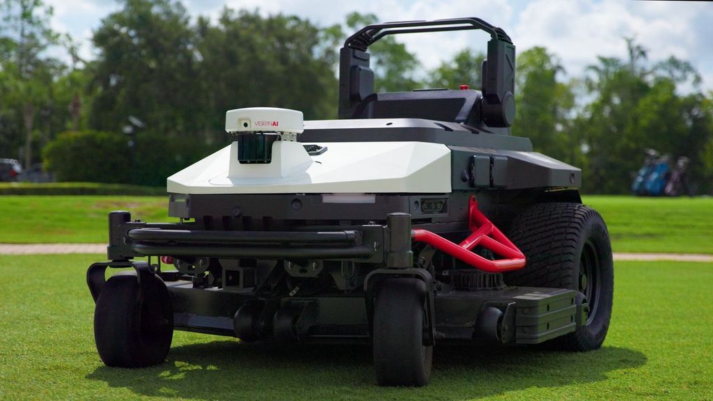Red and white zero-turn radius lawn mower displayed on green grass field with trees in background