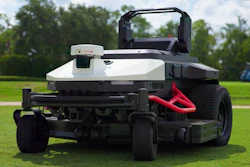 Red and white zero-turn radius lawn mower displayed on green grass field with trees in background