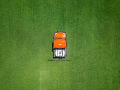 Overhead view of orange and black ride-on lawn mower on green grass