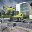 Yellow Liebherr wheeled excavator operating on construction site with modern building in background