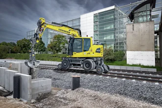 Yellow Liebherr wheeled excavator operating on construction site with modern building in background