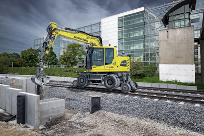 Yellow Liebherr wheeled excavator operating on construction site with modern building in background