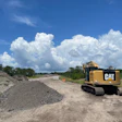 Caterpillar excavator operating at construction site with gravel pile and rural landscape