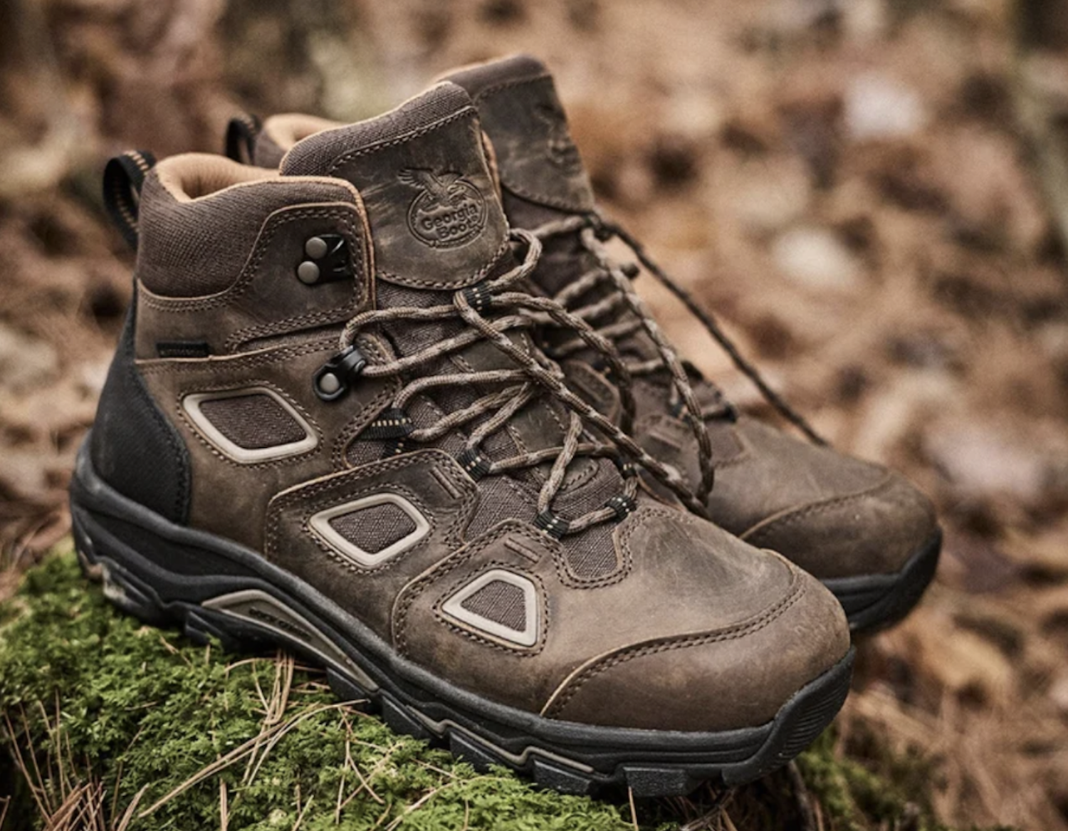 Pair of brown and black hiking boots with laces on rocky, moss-covered ground