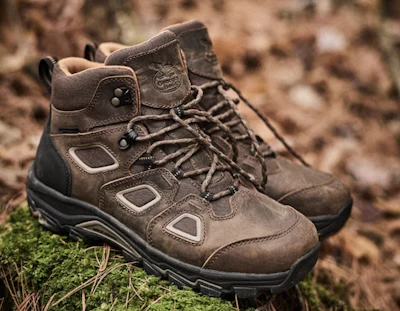 Pair of brown and black hiking boots with laces on rocky, moss-covered ground