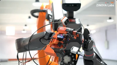 Orange robotic arm with sensors in laboratory setting, ZINOVA Labs branding visible