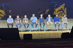 Panel of construction contractors seated on stage during Caterpillar's Tech Days with heavy equipment displayed in the background.