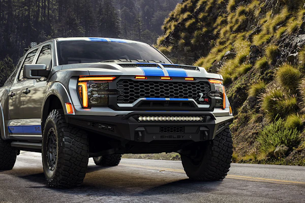 2026 Shelby Ford F-150 Baja Raptor R pickup truck with white and blue racing stripes on forest road