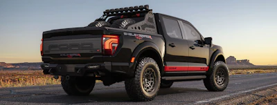 Black Ford Shelby pickup truck with red racing stripes parked on desert highway at sunset