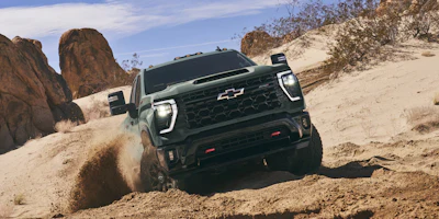 Green Chevrolet pickup truck climbing sandy desert terrain with rocky formations